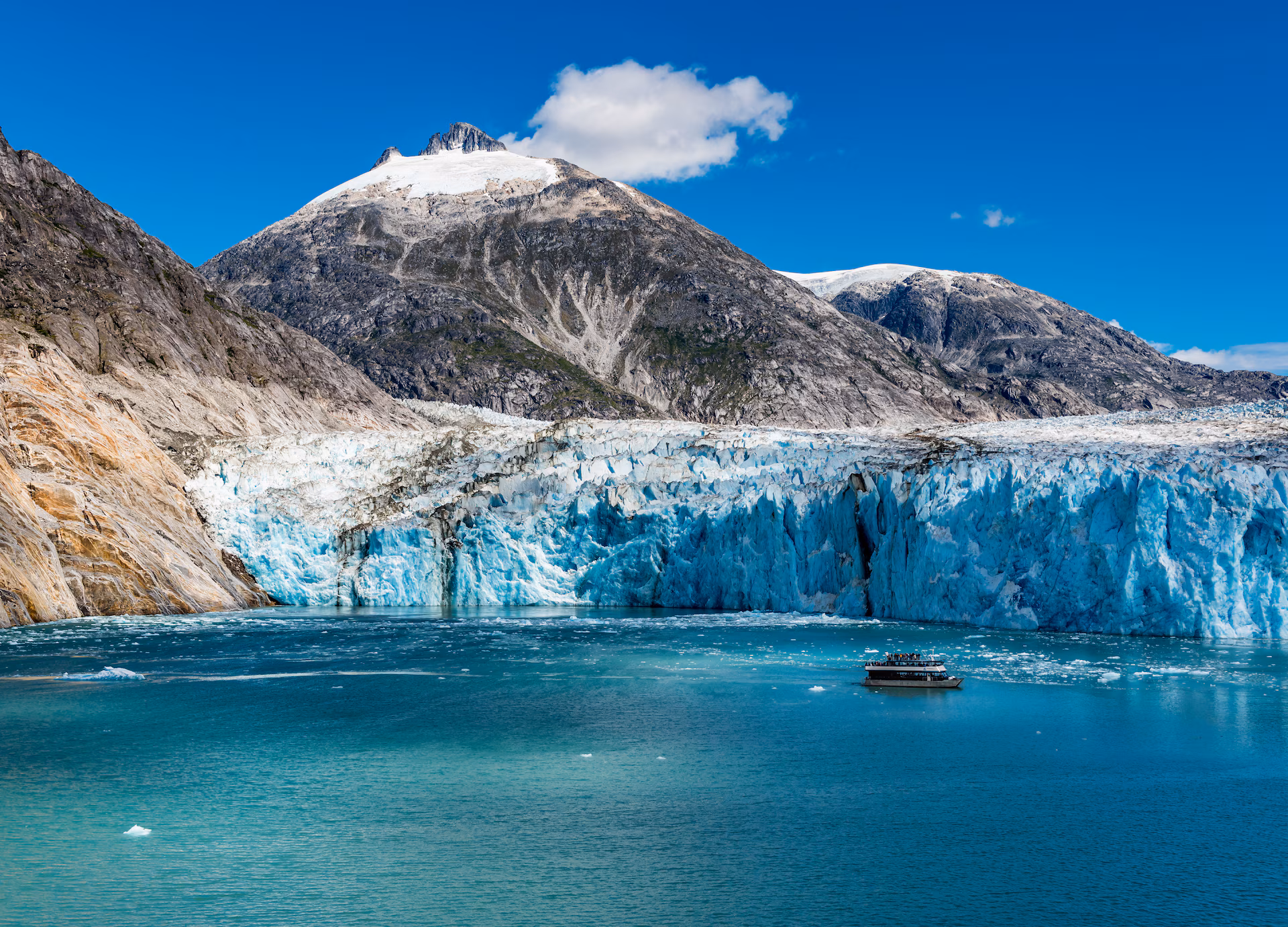 Cruise ship sailing an Alaskan fjord beneath snow-capped mountains